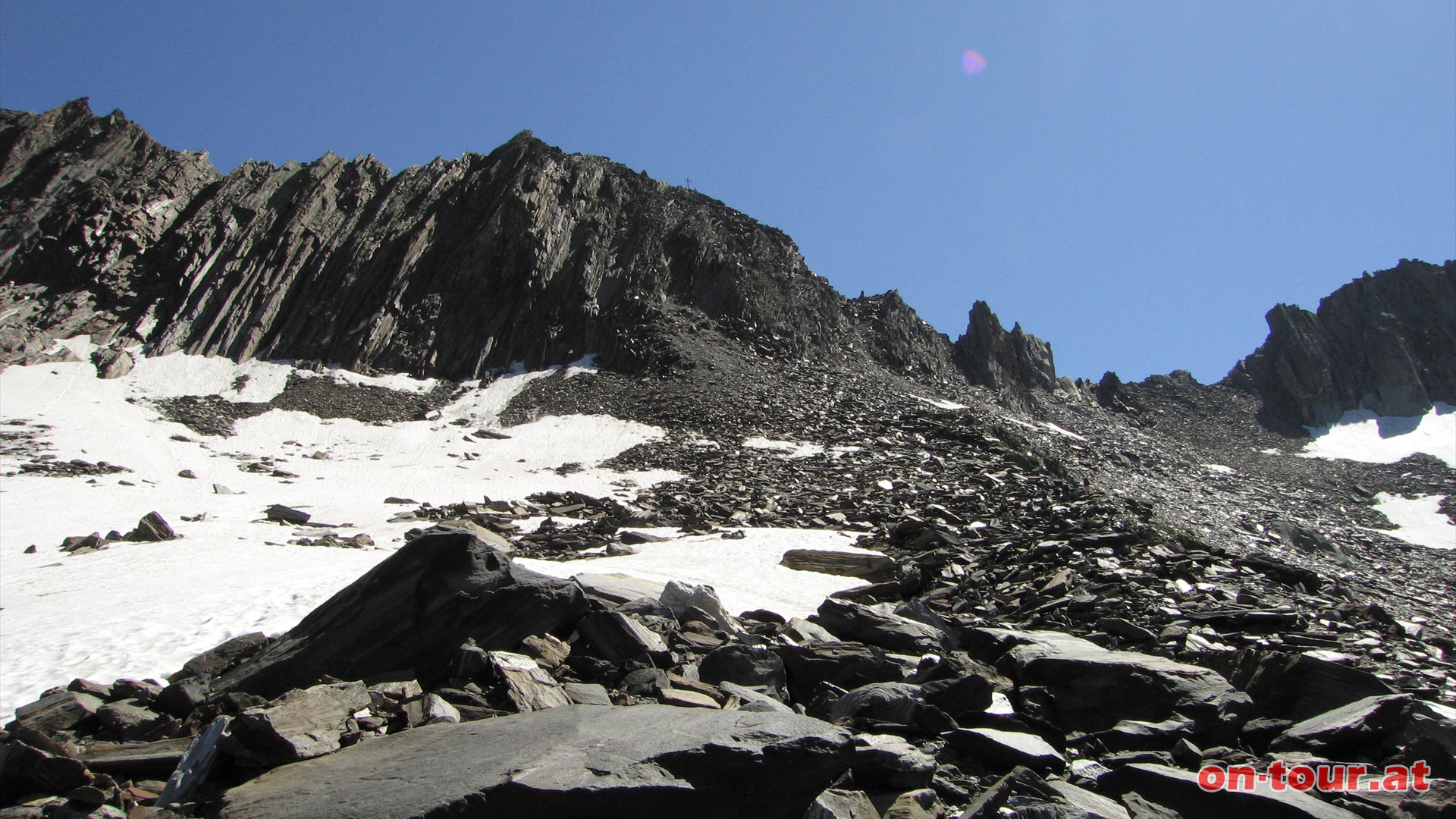 An der Westflanke des Schnbichlerhorns wird der Weg steiler und steiniger. Das Kreuz am Gipfel ist bereits erkennbar.