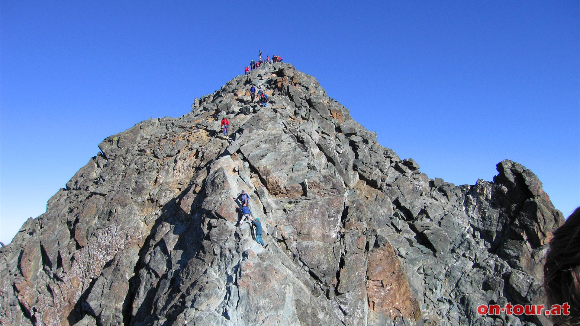 Der Gipfel ist bereits greifbar nahe, doch davor ist noch der Abstieg zur Glocknerscharte zu bewältigen. Die Fixseile sind hilfreich. Die Scharte ist über einen schmalen Fußweg zu begehen. Rechts führt die Pallavicini-Rinne 1200 Meter steilst hinunter und links die Südrinne mit 800 Höhenmeter bis zum Ködnitzkees.